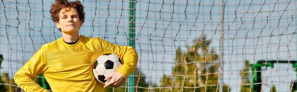 Um jovem segura com confiança uma bola de futebol na frente de uma rede, pronta para dar um tiro. A antecipação e intensidade do momento são palpáveis quando ele se prepara para apontar para o objetivo. — Fotografia de Stock