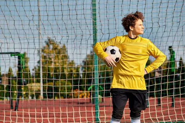 Мужчина в яркой желтой рубашке уверенно держит футбольный мяч, демонстрируя свою страсть к спорту. — стоковое фото