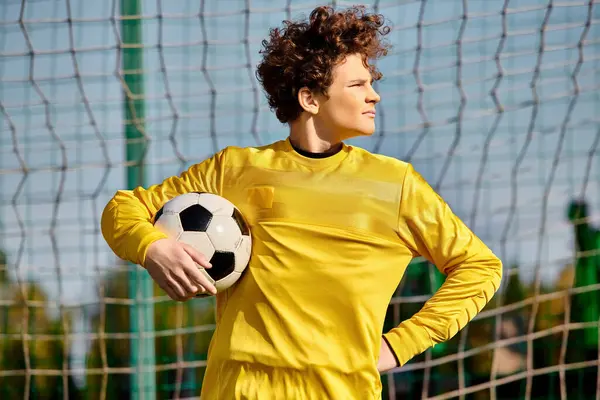 Мужчина в ярко-желтой форме уверенно держит футбольный мяч, источая страсть и мастерство для спорта. — стоковое фото