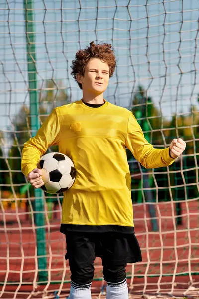 A young man stands confidently, holding a soccer ball in front of a net. The determination in his eyes is evident as he prepares to take a shot, showcasing his passion for the sport and his goal-scoring abilities. — Stock Photo