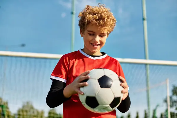Un jeune garçon se tient devant un but, tenant un ballon de football. Il semble concentré et déterminé, prêt à tirer sur le but. La scène capture l'essence de la passion et de l'excitation pour le sport du football. — Photo de stock