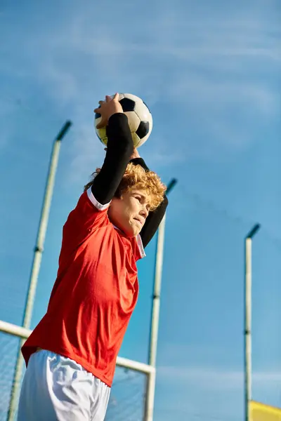 Un hombre joven levanta alegremente una pelota de fútbol triunfante en el cielo, celebrando su destreza atlética y su amor por el deporte. Su expresión emana pura euforia y pasión por el juego. - foto de stock
