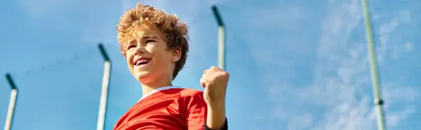 Ein Junge im leuchtend roten Hemd hält selbstbewusst einen Baseballschläger mit entschlossenem Gesichtsausdruck in der Hand. Er steht bereit, zeigt seine Leidenschaft für den Sport und seine Bereitschaft, zu schwingen. — Stockfoto