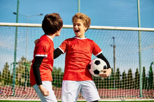 Due giovani uomini in abbigliamento atletico in piedi fianco a fianco su un campo di calcio, mostrando lavoro di squadra e cameratismo. — Foto stock