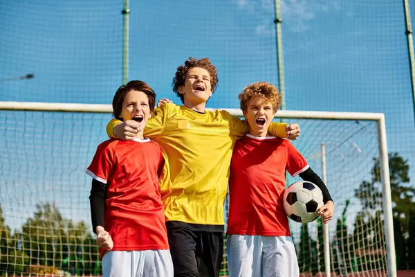 A group of young boys, all dressed in soccer jerseys, stand closely together in unity on a green soccer field. Each boy is looking in different directions, some talking and laughing, while others are focused and ready to play. — Stock Photo