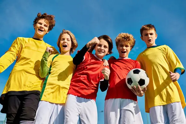 Un groupe vivant de jeunes individus se tiennent étroitement ensemble, tenant un ballon de football avec enthousiasme et camaraderie. Leurs visages reflètent l'excitation et l'unité alors qu'ils se préparent pour un match amical. — Photo de stock