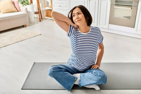 Mature woman in cozy homewear practicing yoga on a mat in her living room. — Stock Photo