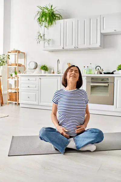 Una mujer madura practica yoga sobre una esterilla en su acogedora cocina. - foto de stock