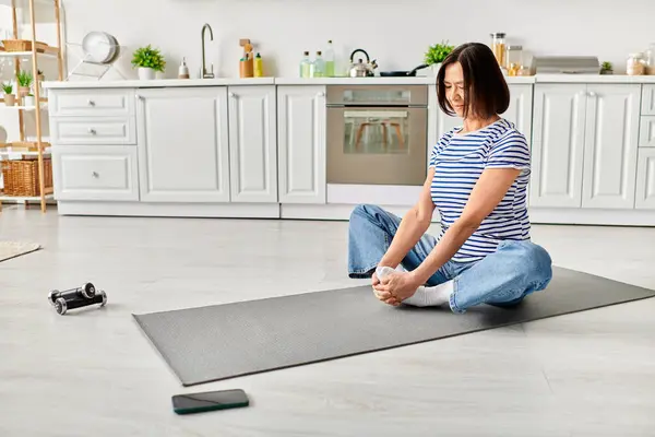 A mature beautiful woman in cozy homewear practices yoga on a mat in the kitchen. — Stock Photo