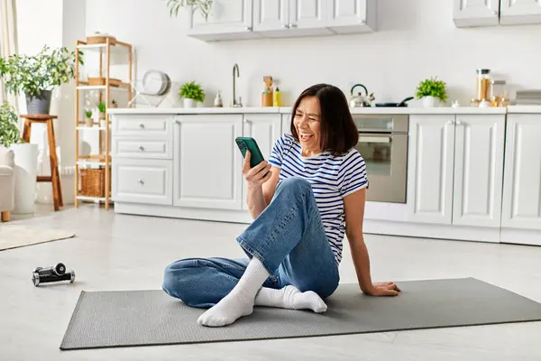 Взрослая красивая женщина в уютной домашней одежде сидит на полу, используя мобильный телефон. — стоковое фото