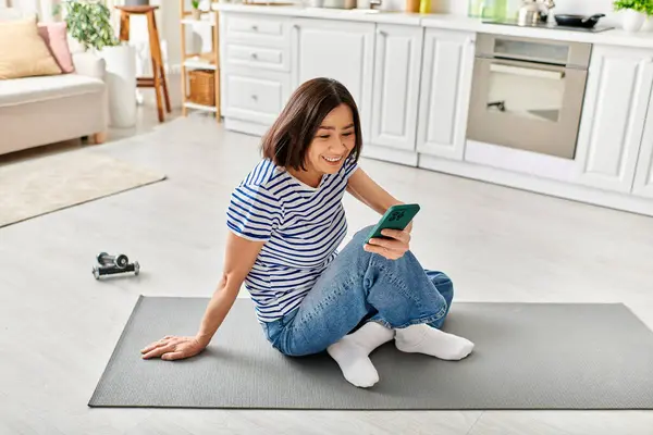 Woman in cozy homewear sitting on floor, using cell phone. — Stock Photo