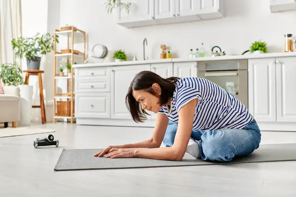 Mature woman in cozy homewear kneels on yoga mat in her living room. — Stock Photo