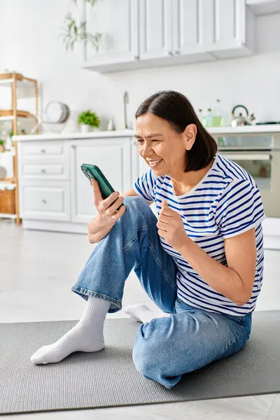 Взрослая женщина в уютном домашнем платье сидит на полу, поглощенная своим телефоном. — стоковое фото