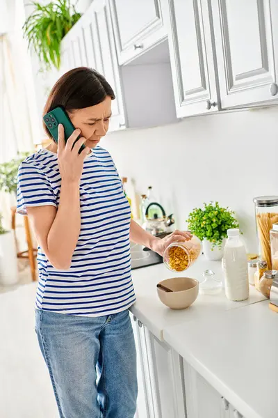 A mature woman in cozy homewear talking on a cell phone in the kitchen. — Stock Photo