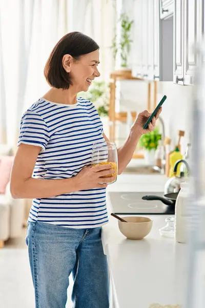 Жінка в затишному домашньому вбранні насолоджується склянкою апельсинового соку на кухні. — стокове фото