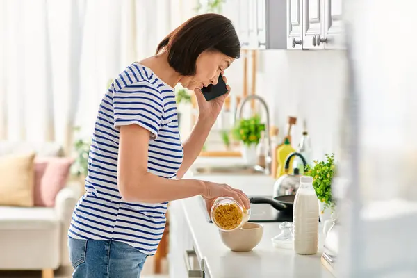 Eine reife Frau in kuscheliger Homewear plaudert in der Küche auf einem Handy. — Stockfoto
