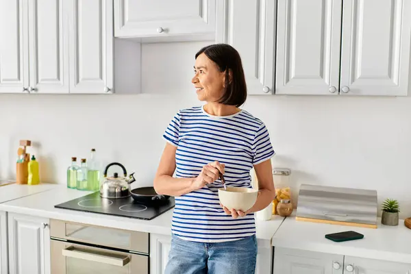Жінка в затишному вбранні стоїть на кухні, тримаючи чашу. — стокове фото