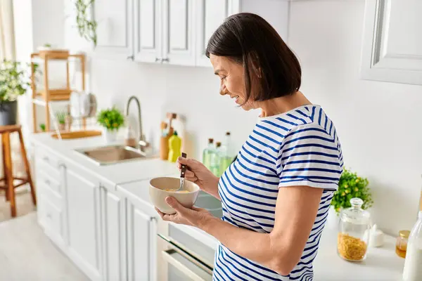 Woman in cozy homewear holding a bowl of food in a kitchen. — Stock Photo