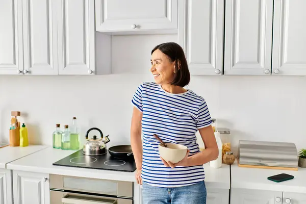 Mujer madura en ropa de casa acogedora sosteniendo un tazón en su cocina. - foto de stock