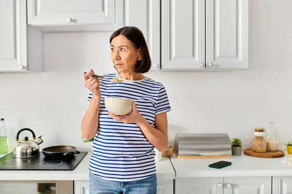 Stylish woman in cozy attire holding a bowl of food in a warm kitchen. — Stock Photo