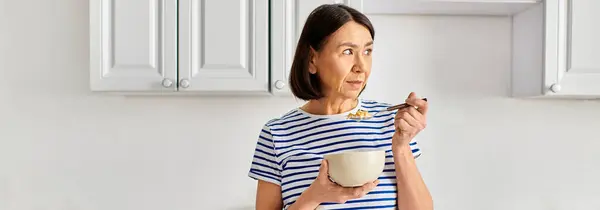 A mature woman in cozy attire holding a glass of milk and a spoon. — Stock Photo