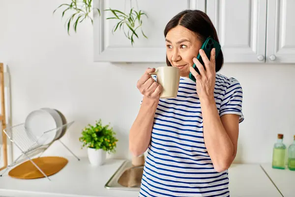 Mujer en ropa de casa acogedora sosteniendo la taza de café, hablando por teléfono. - foto de stock