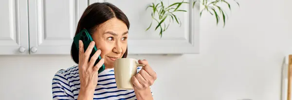 Una mujer en acogedora multitarea de ropa de casa con un teléfono celular y una taza de café. - foto de stock