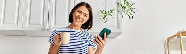 A woman in cozy homewear multitasking with a cup of coffee and a cell phone. — Stock Photo