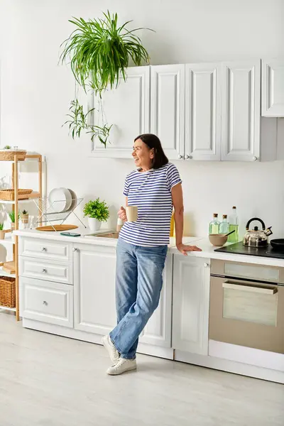 Une femme mûre en tenue confortable debout dans une cuisine, à côté d'un évier. — Photo de stock