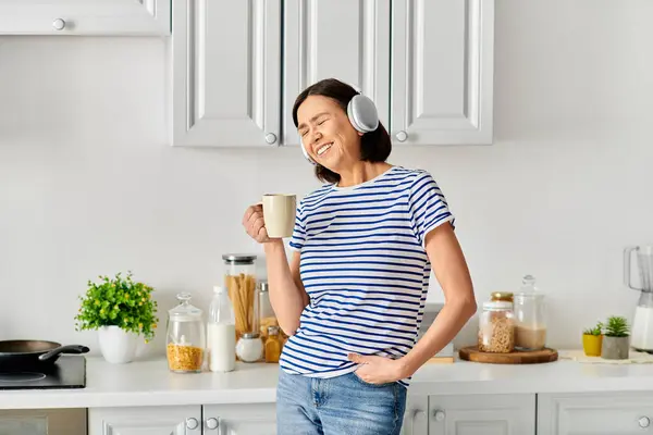 Une femme en tenue confortable debout dans une cuisine, tenant une tasse de café. — Photo de stock