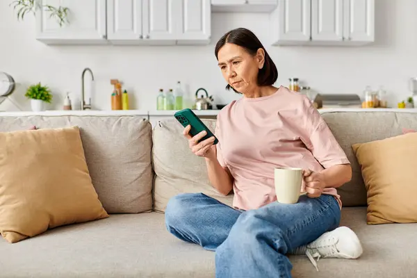 A cozy woman engrossed in her phone on a couch. — Stock Photo