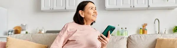 A mature woman in a pink shirt holds a green object, embodying tranquility at home. — Stock Photo