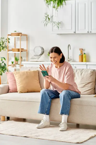 A mature woman in homewear sits on a couch, engrossed in a book. — Stock Photo