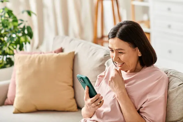 A woman in cozy homewear engrossed in her phone while sitting on a couch. — Stock Photo