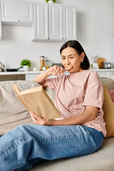 Eine Frau in kuscheliger Kleidung sitzt auf einer Couch, ganz in ein Buch vertieft. — Stockfoto