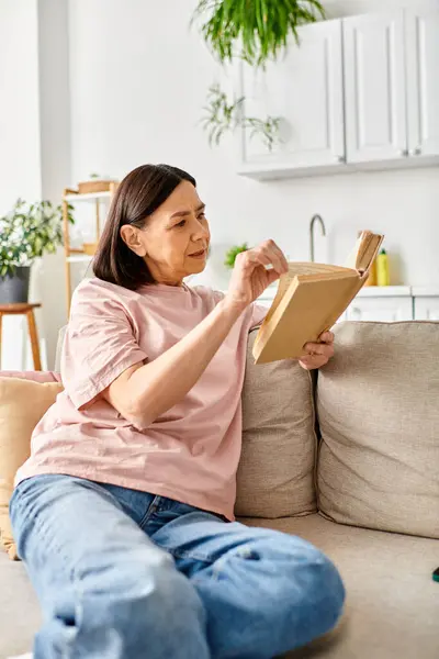 Eine reife Frau vertieft in ein Buch, während sie zu Hause auf einer gemütlichen Couch sitzt. — Stockfoto