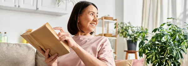 A mature woman in cozy homewear sitting on a couch, holding a box. — Stock Photo
