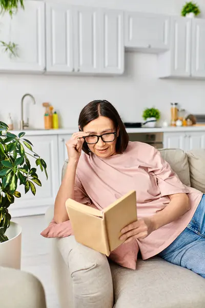 A mature woman in cozy homewear reads a book on a couch. — Stock Photo