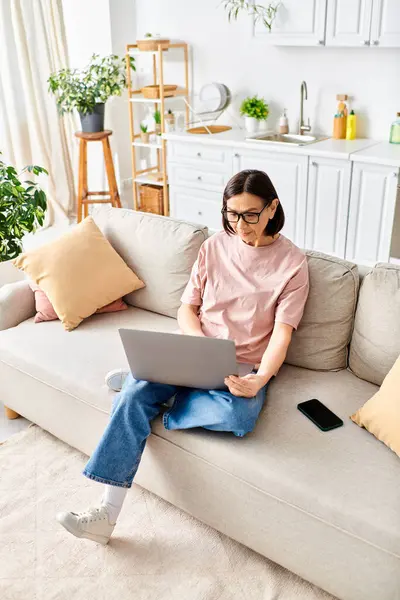 Una donna matura in abbigliamento accogliente, assorto nel suo computer portatile mentre seduto su un divano. — Foto stock