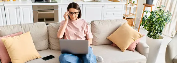 A mature woman in cozy homewear sits on a couch, engrossed in using a laptop. — Stock Photo
