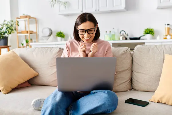 A mature woman in cozy attire sits comfortably on a couch, absorbed in her laptop. — Stock Photo