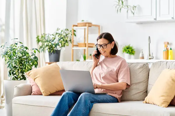 A woman in casual attire using a laptop on a couch. — Stock Photo