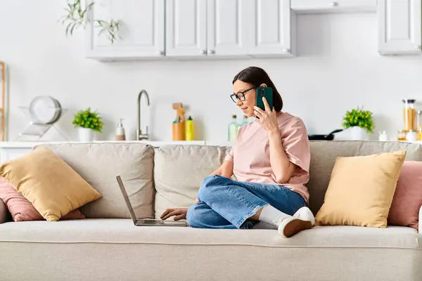 A mature woman in cozy homewear sitting on a couch, engaged in a phone conversation. — Stock Photo
