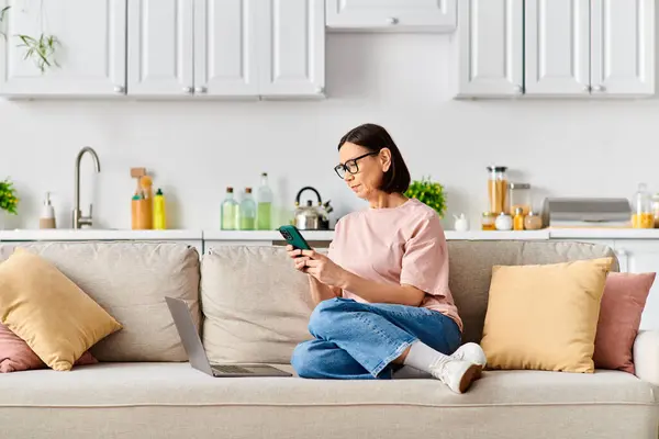 Mature woman in cozy homewear sitting on couch, focused on tablet screen. — Stock Photo