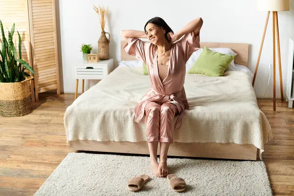 Mature woman in homewear sitting on bed in bedroom. — Stock Photo