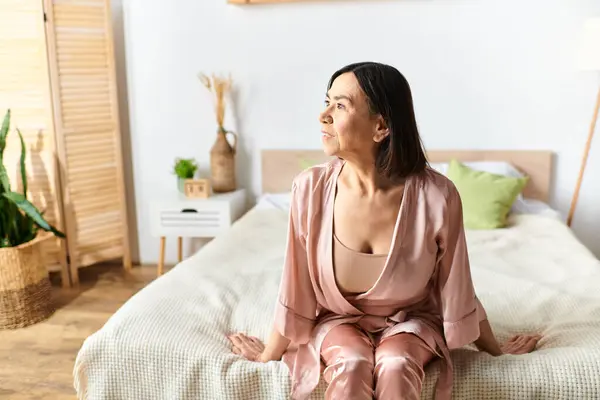 A mature woman in cozy homewear relaxing on a bed in a serene room. — Stock Photo