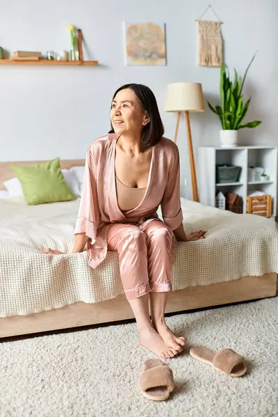 A mature woman in cozy homewear sits atop a bed in a bedroom — Stock Photo