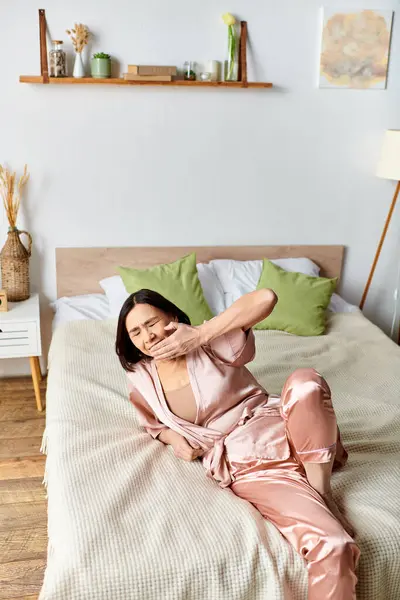 Eine reife Frau im rosa Pyjama liegt friedlich auf einem gemütlichen Bett. — Stockfoto