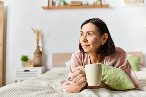 Uma mulher madura descansando em uma cama com uma xícara de café em roupa de casa aconchegante. — Fotografia de Stock