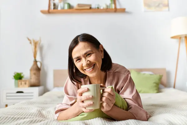 A woman in cozy homewear laying on a bed, peacefully holding a cup. — Stock Photo